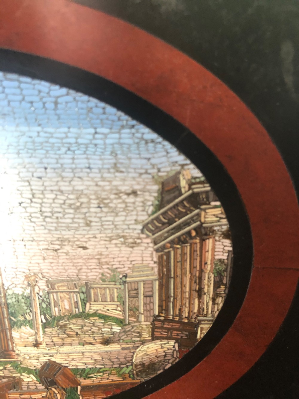 A cartouche-shaped black marble paperweight with a terracotta-coloured inlay ring surrounding a central oval micro-mosaic depicting classical Roman architectural ruins. View V