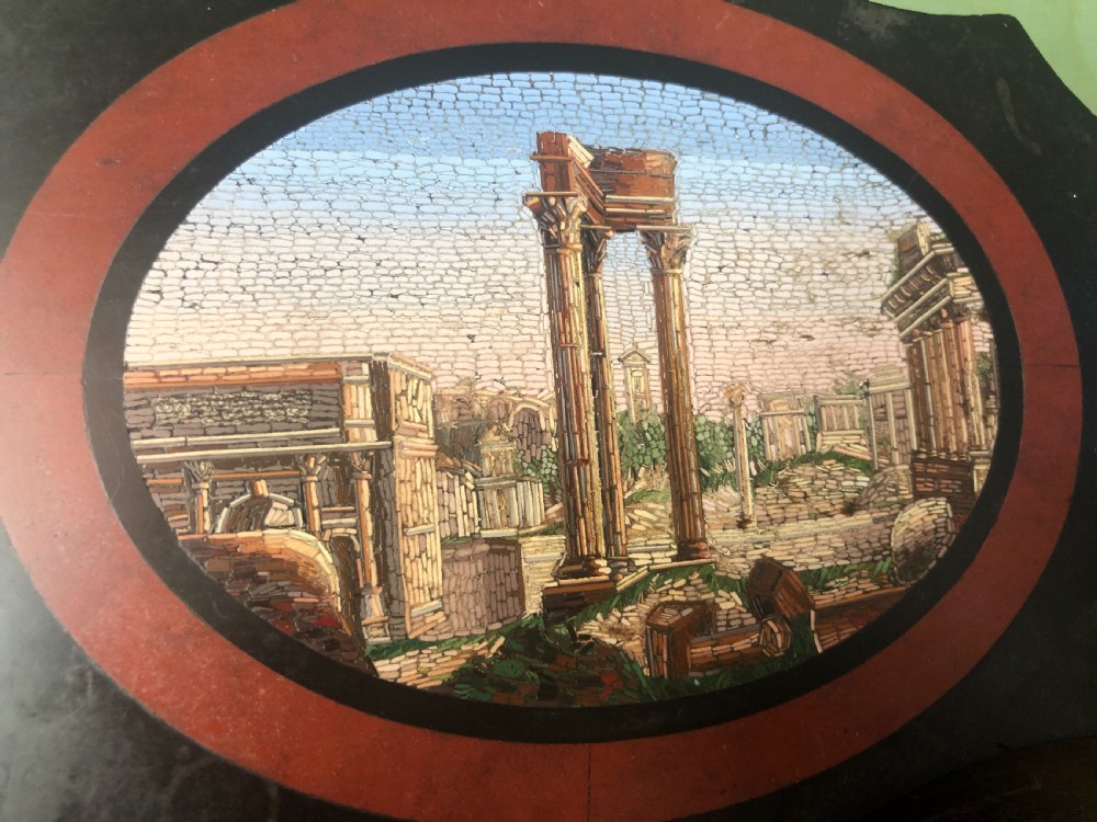 A cartouche-shaped black marble paperweight with a terracotta-coloured inlay ring surrounding a central oval micro-mosaic depicting classical Roman architectural ruins. View IX