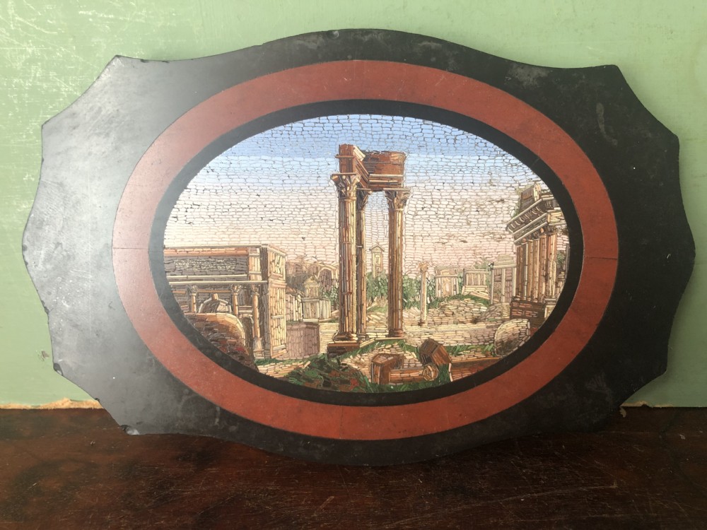 A cartouche-shaped black marble paperweight with a terracotta-coloured inlay ring surrounding a central oval micro-mosaic depicting classical Roman architectural ruins. View XVIII