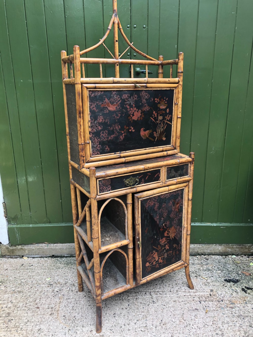 A late 19th-century bamboo escritoire cabinet featuring a pagoda-shaped top finial, a lacquered drop-front writing slope, side shelves, and a lower lacquered cupboard door decorated with floral motifs.