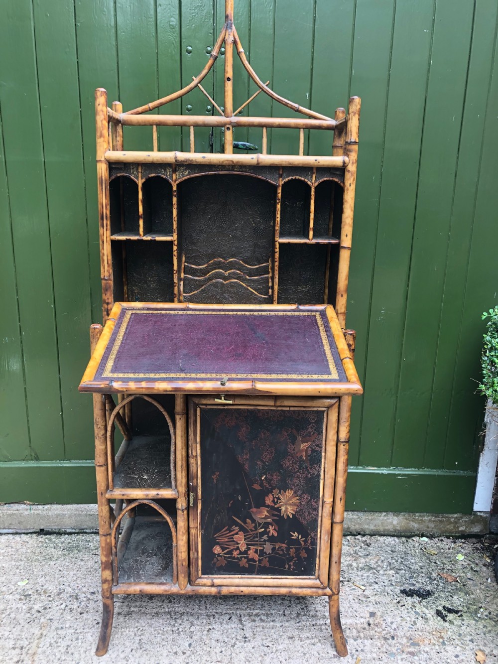 A late 19th-century bamboo escritoire cabinet featuring a pagoda-shaped top finial, a lacquered drop-front writing slope, side shelves, and a lower lacquered cupboard door decorated with floral motifs. View V