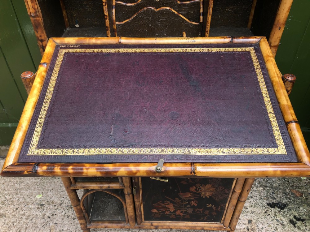 A late 19th-century bamboo escritoire cabinet featuring a pagoda-shaped top finial, a lacquered drop-front writing slope, side shelves, and a lower lacquered cupboard door decorated with floral motifs. View VI