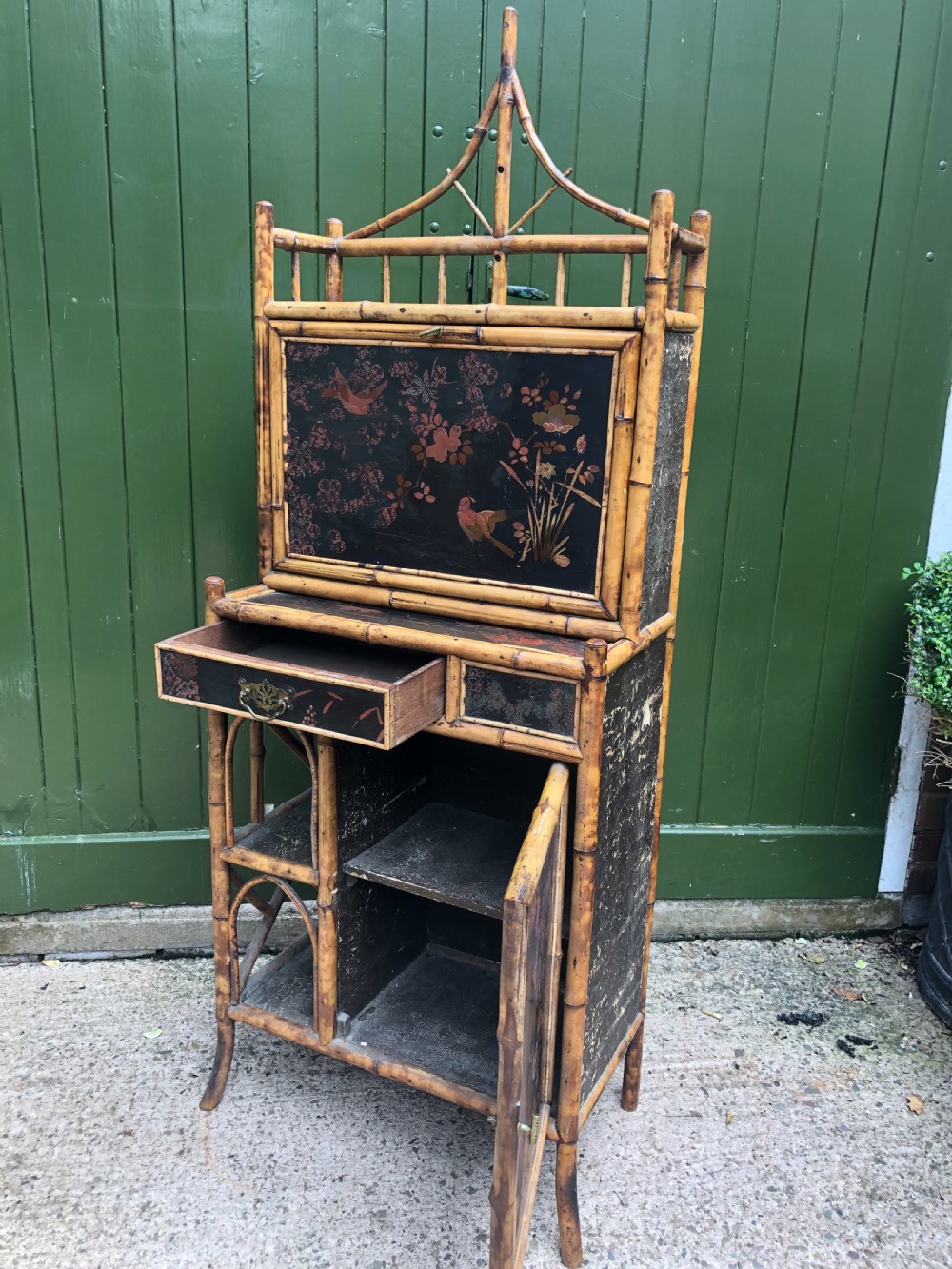 A late 19th-century bamboo escritoire cabinet featuring a pagoda-shaped top finial, a lacquered drop-front writing slope, side shelves, and a lower lacquered cupboard door decorated with floral motifs. View VIII
