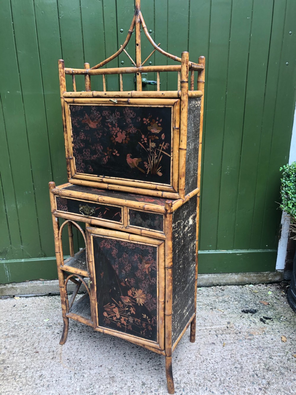 A late 19th-century bamboo escritoire cabinet featuring a pagoda-shaped top finial, a lacquered drop-front writing slope, side shelves, and a lower lacquered cupboard door decorated with floral motifs. View X