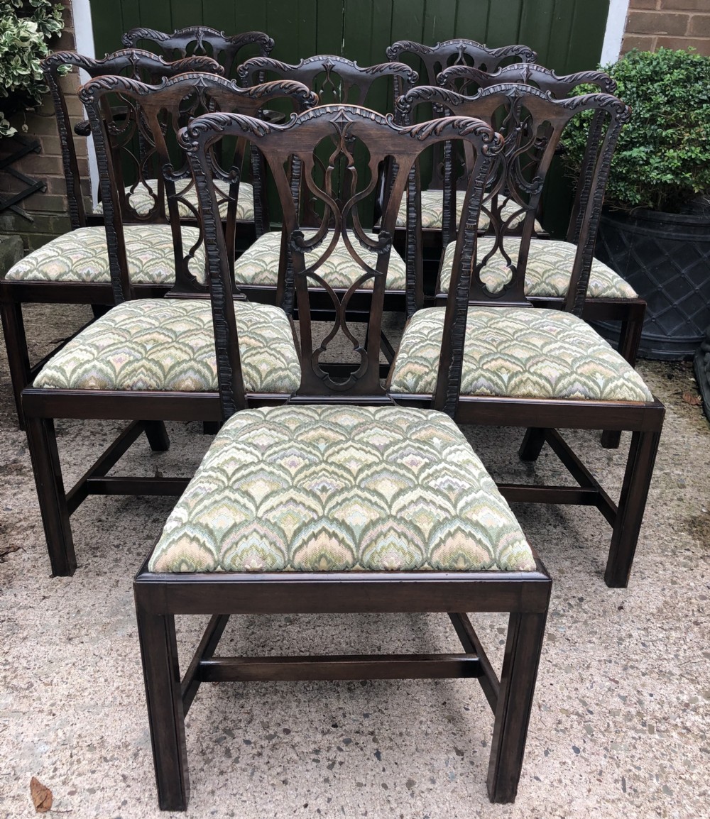 A set of eight carved mahogany Chippendale style dining chairs with decorative pierced back splats and patterned upholstered seats.