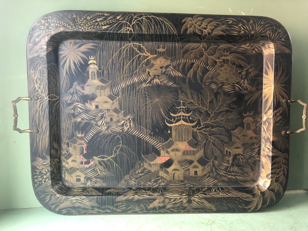 A rectangular black lacquered Regency papier-mache tray featuring gilded chinoiserie landscape decoration and two brass side handles.