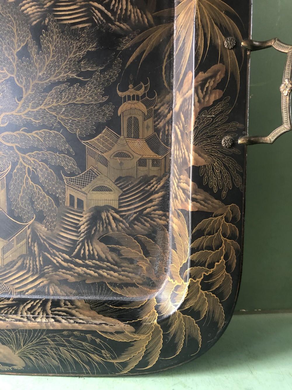 A rectangular black lacquered Regency papier-mache tray featuring gilded chinoiserie landscape decoration and two brass side handles. View X