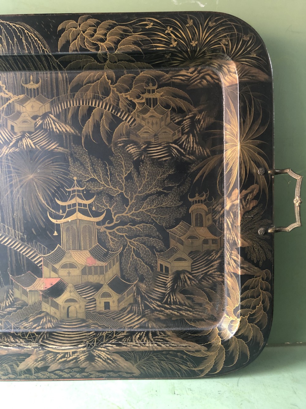 A rectangular black lacquered Regency papier-mache tray featuring gilded chinoiserie landscape decoration and two brass side handles. View XV