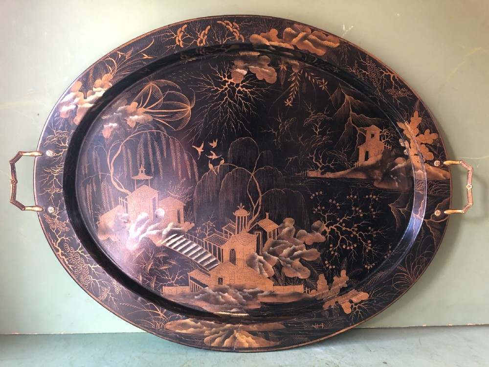 An oval black papier-mache tray featuring detailed gold chinoiserie landscape decoration and two side handles. View II