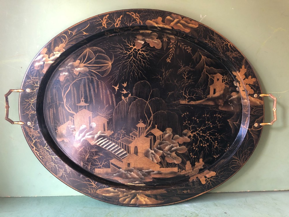 An oval black papier-mache tray featuring detailed gold chinoiserie landscape decoration and two side handles. View III