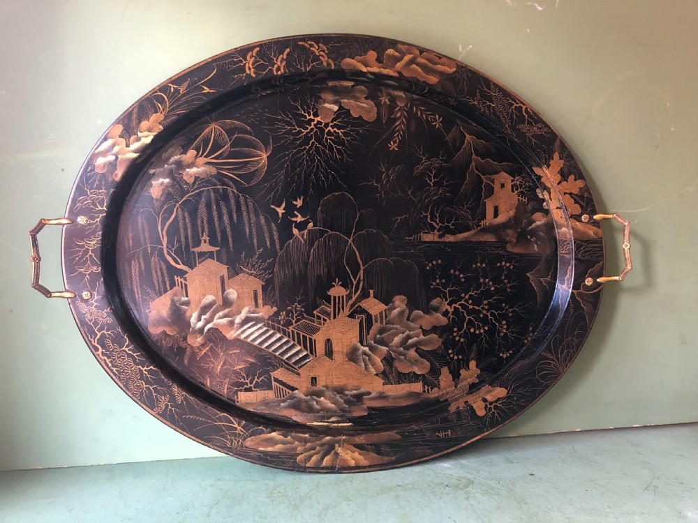 An oval black papier-mache tray featuring detailed gold chinoiserie landscape decoration and two side handles. View VI