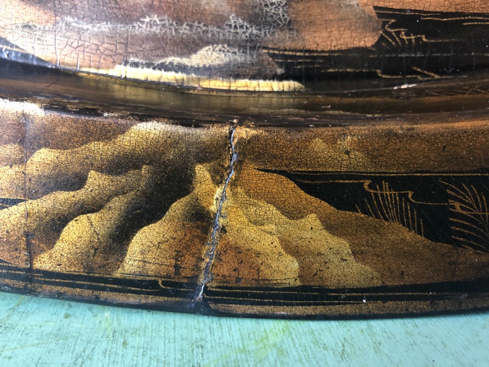 An oval black papier-mache tray featuring detailed gold chinoiserie landscape decoration and two side handles. View IX