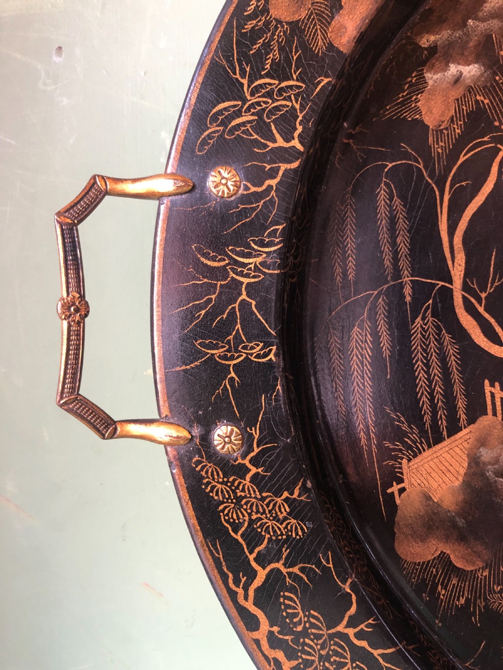 An oval black papier-mache tray featuring detailed gold chinoiserie landscape decoration and two side handles. View XIII