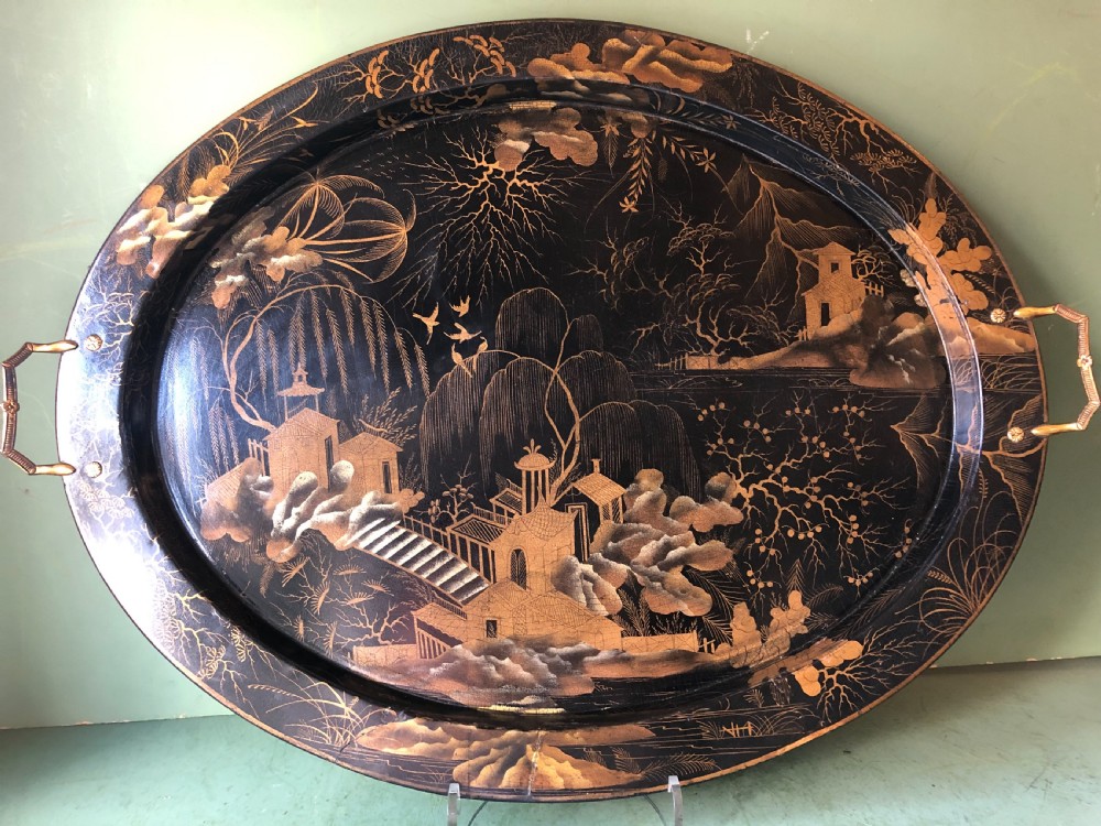 An oval black papier-mache tray featuring detailed gold chinoiserie landscape decoration and two side handles. View XV