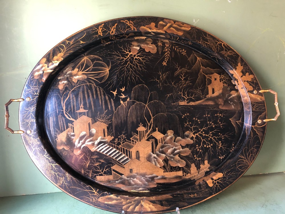 An oval black papier-mache tray featuring detailed gold chinoiserie landscape decoration and two side handles. View XVI