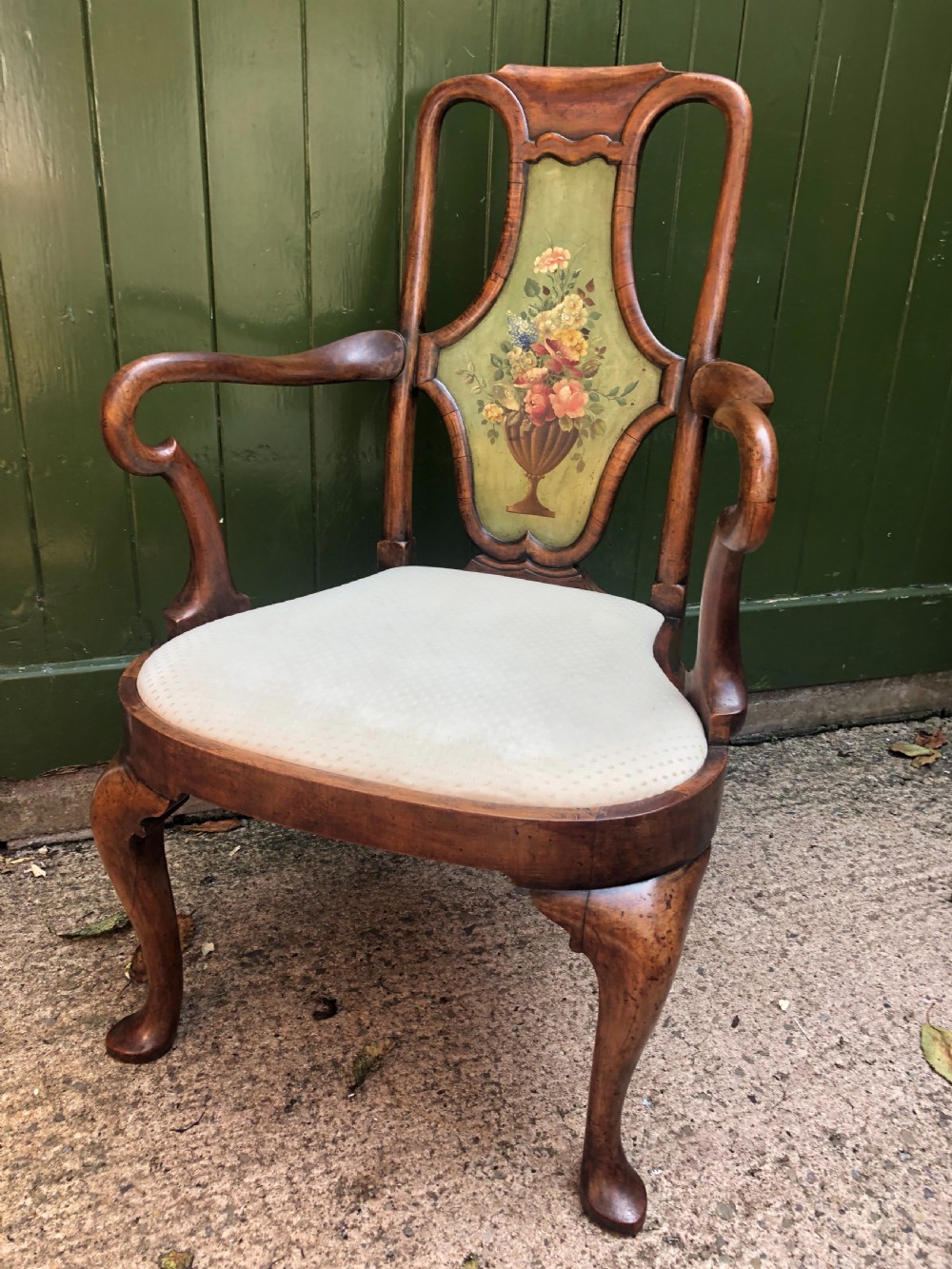 Early 20th-century Queen Anne revival walnut armchair featuring a painted floral splat back, carved armrests, cabriole legs, and cream upholstery.