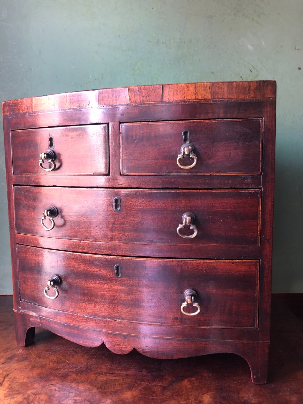 An early nineteenth-century miniature mahogany bow-front chest of drawers featuring brass ring handles and keyholes.