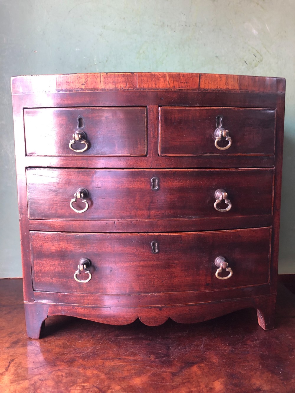 An early nineteenth-century miniature mahogany bow-front chest of drawers featuring brass ring handles and keyholes. View III