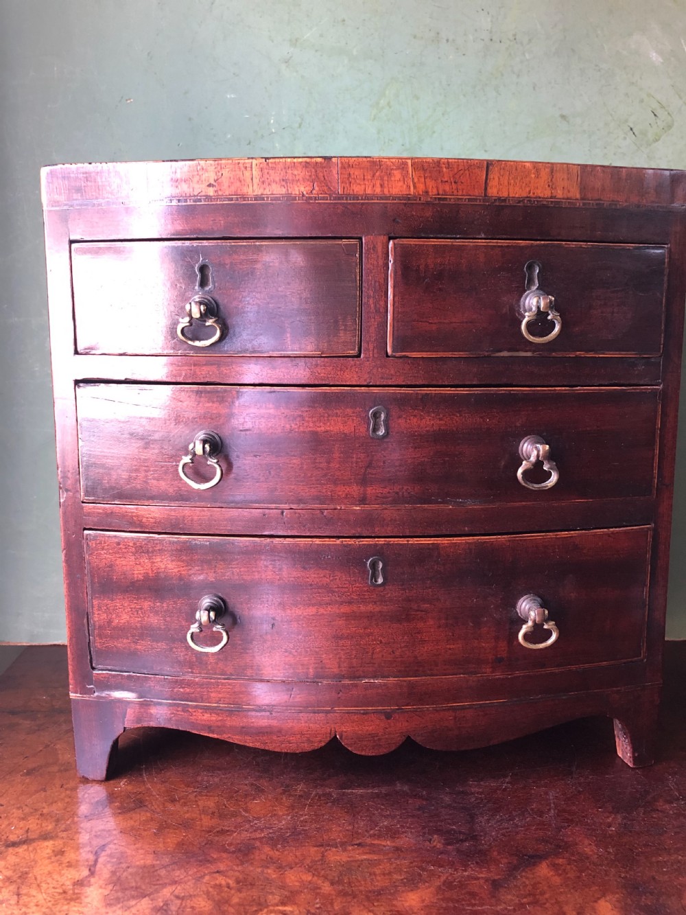 An early nineteenth-century miniature mahogany bow-front chest of drawers featuring brass ring handles and keyholes. View VI