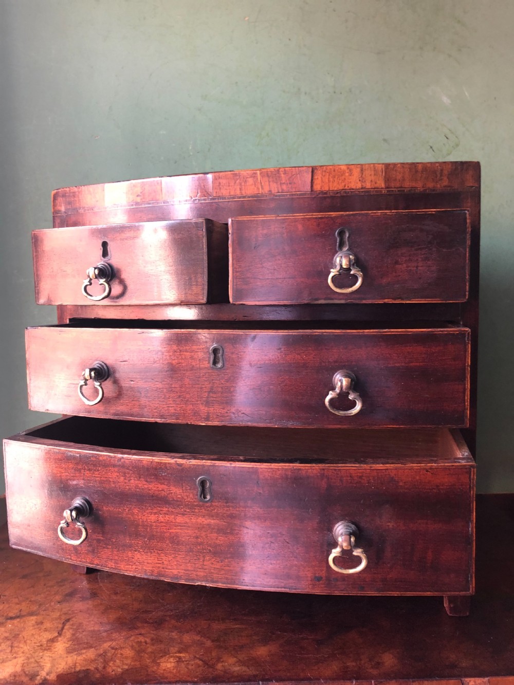 An early nineteenth-century miniature mahogany bow-front chest of drawers featuring brass ring handles and keyholes. View VIII
