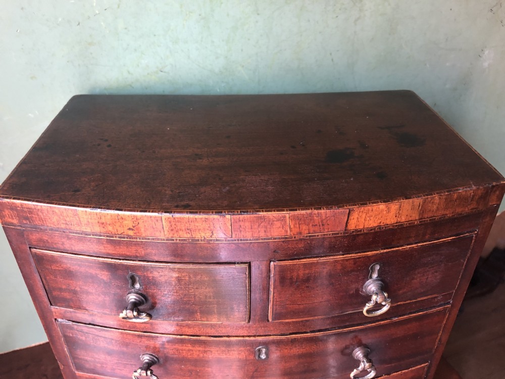 An early nineteenth-century miniature mahogany bow-front chest of drawers featuring brass ring handles and keyholes. View XIII