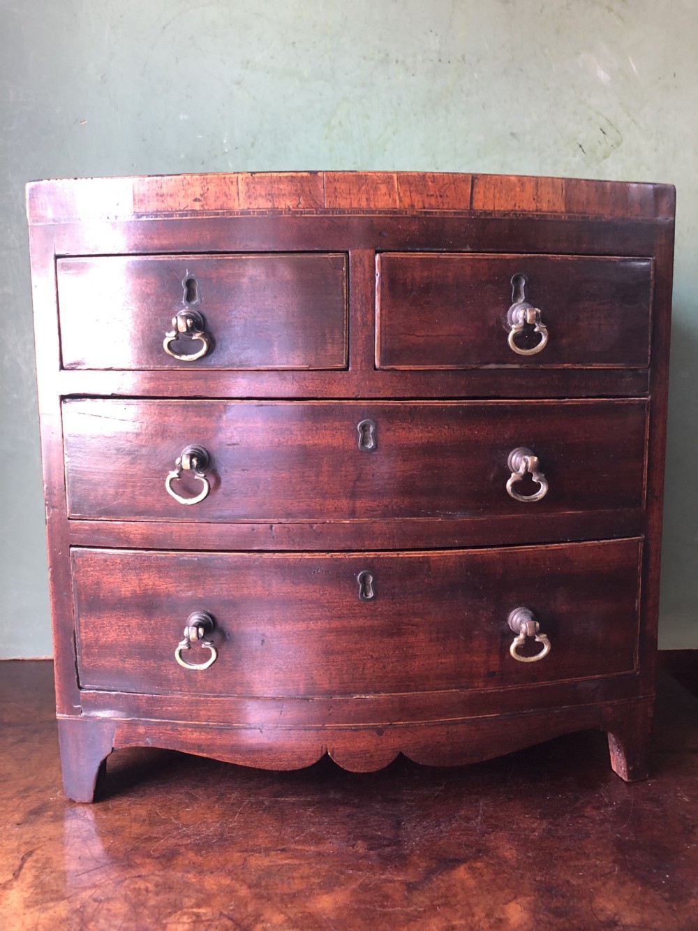 An early nineteenth-century miniature mahogany bow-front chest of drawers featuring brass ring handles and keyholes. View XV