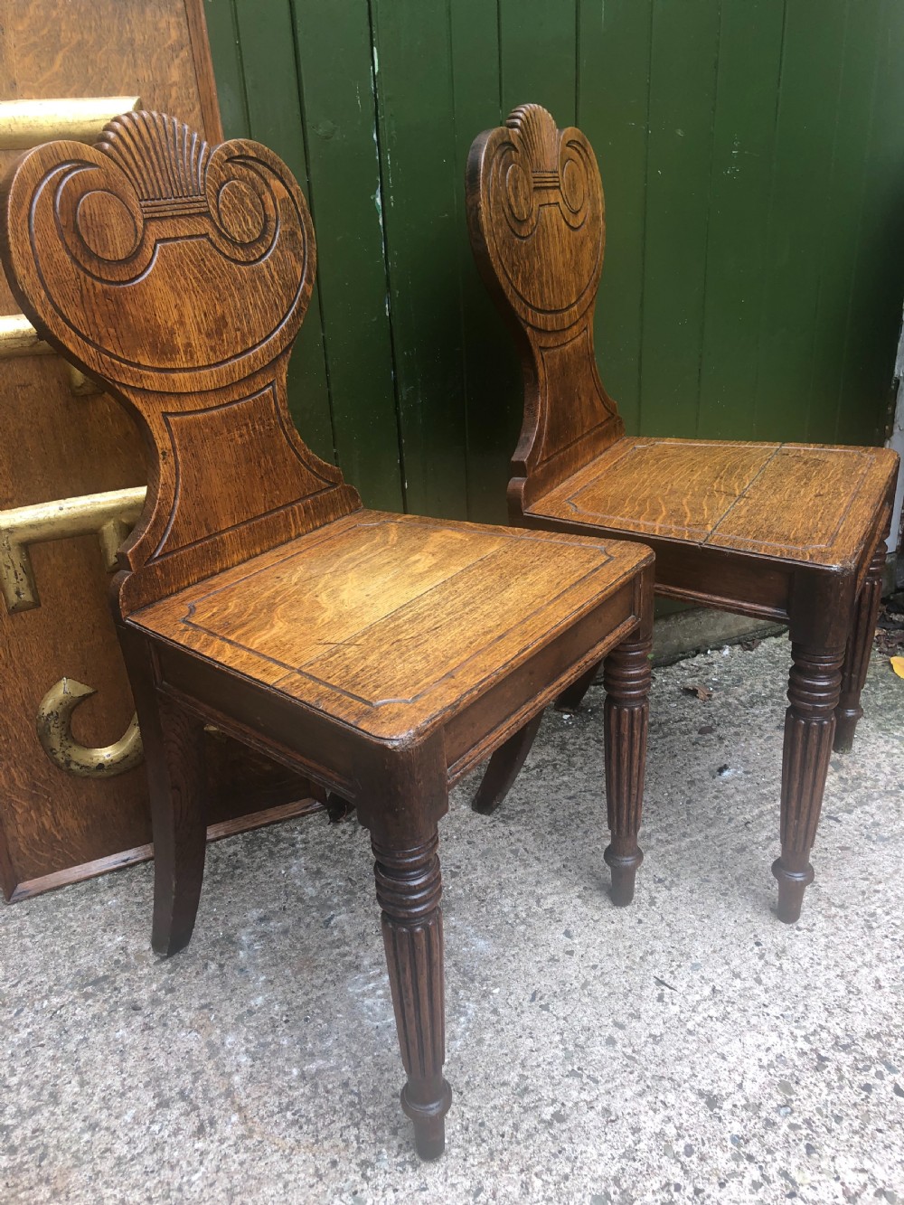 A pair of early nineteenth-century Regency oak hall chairs featuring carved scroll backs with shell motifs, solid timber seats, and reeded front legs. View III