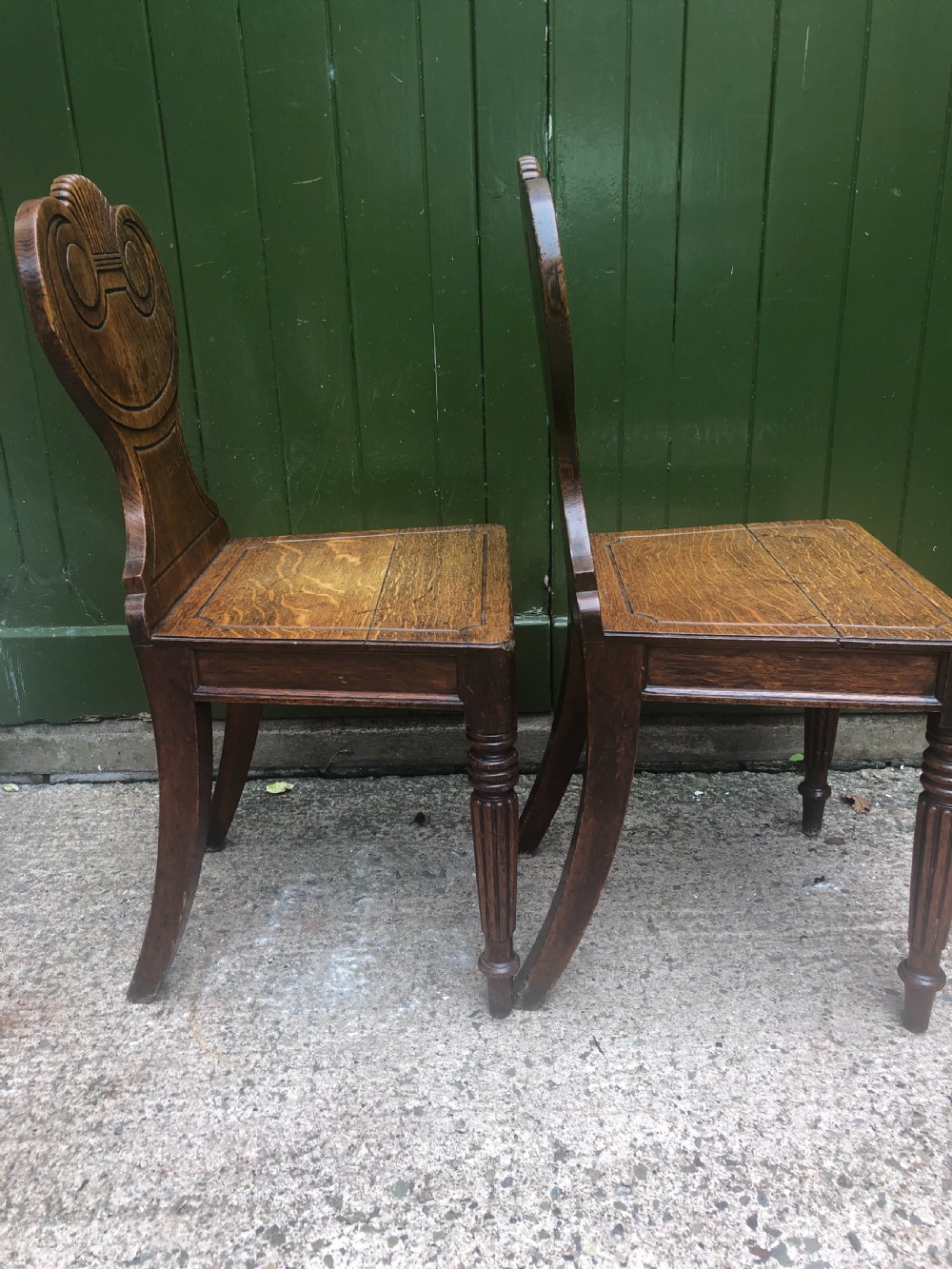 A pair of early nineteenth-century Regency oak hall chairs featuring carved scroll backs with shell motifs, solid timber seats, and reeded front legs. View IV