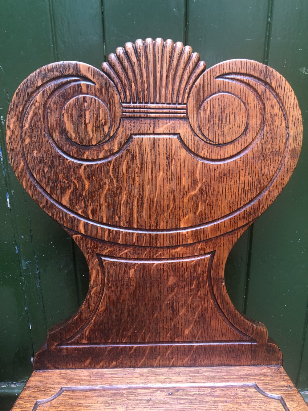 A pair of early nineteenth-century Regency oak hall chairs featuring carved scroll backs with shell motifs, solid timber seats, and reeded front legs. View IX