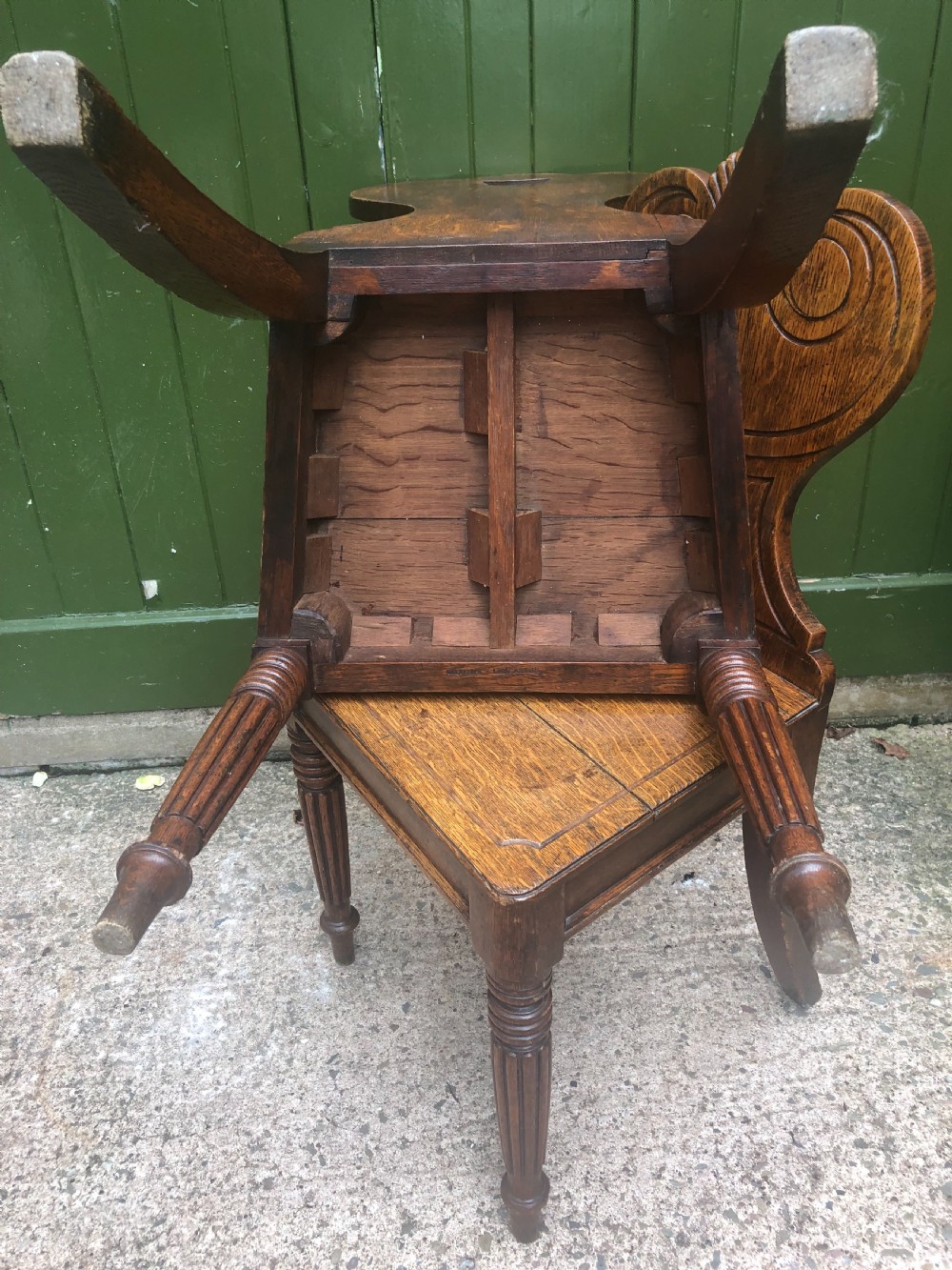 A pair of early nineteenth-century Regency oak hall chairs featuring carved scroll backs with shell motifs, solid timber seats, and reeded front legs. View XIV