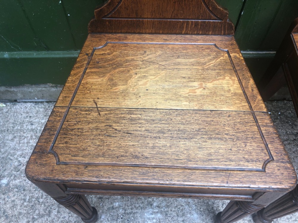 A pair of early nineteenth-century Regency oak hall chairs featuring carved scroll backs with shell motifs, solid timber seats, and reeded front legs. View VI
