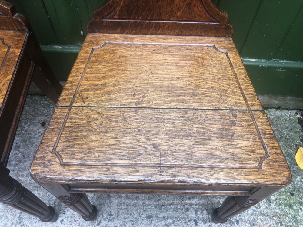 A pair of early nineteenth-century Regency oak hall chairs featuring carved scroll backs with shell motifs, solid timber seats, and reeded front legs. View VII