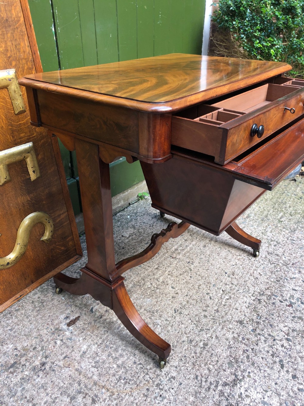 A George IV mahogany work table featuring a single drawer with turned knobs, a tapered lower well, carved trestle supports, and brass castors. View V