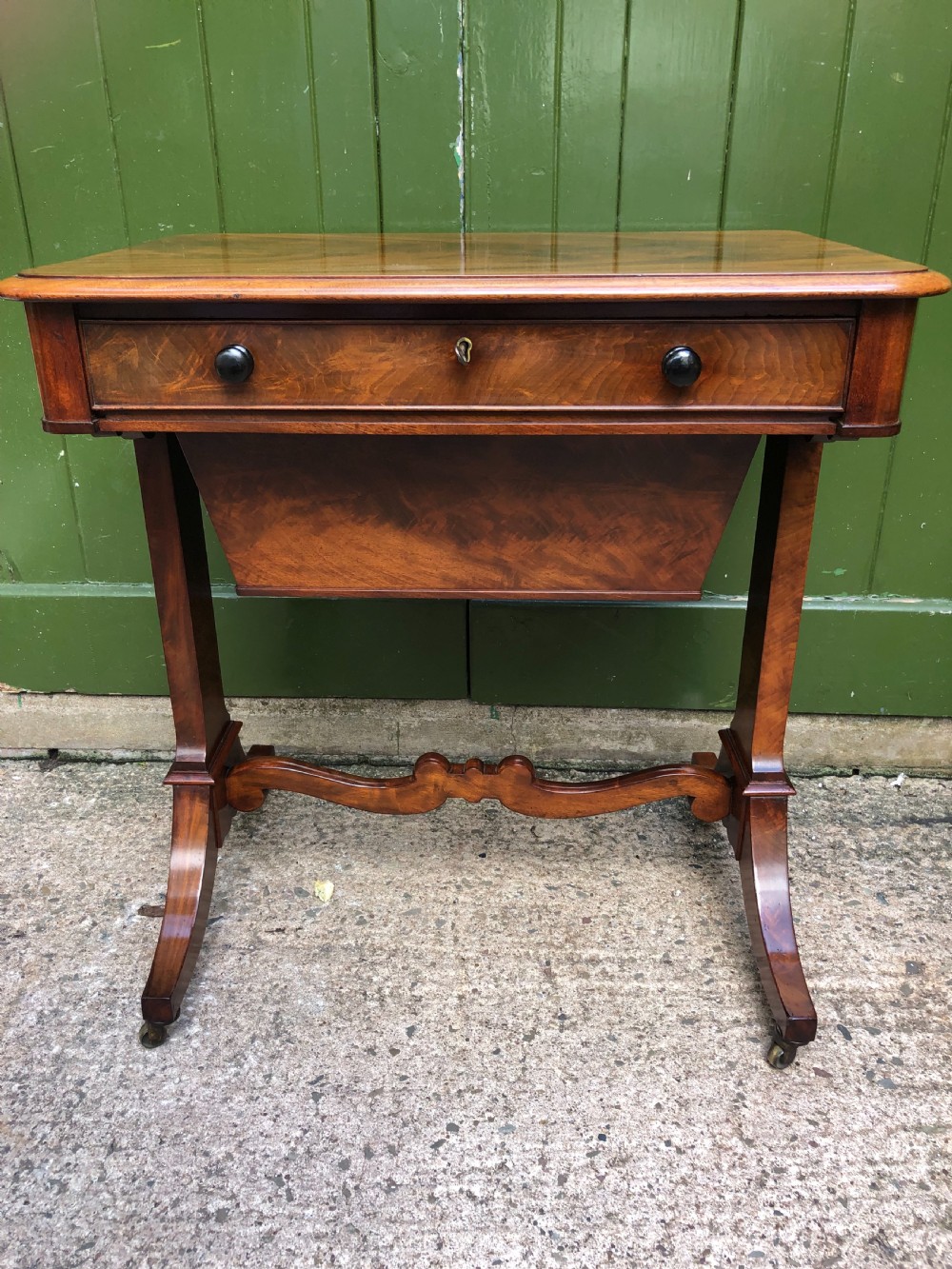 A George IV mahogany work table featuring a single drawer with turned knobs, a tapered lower well, carved trestle supports, and brass castors. View VII