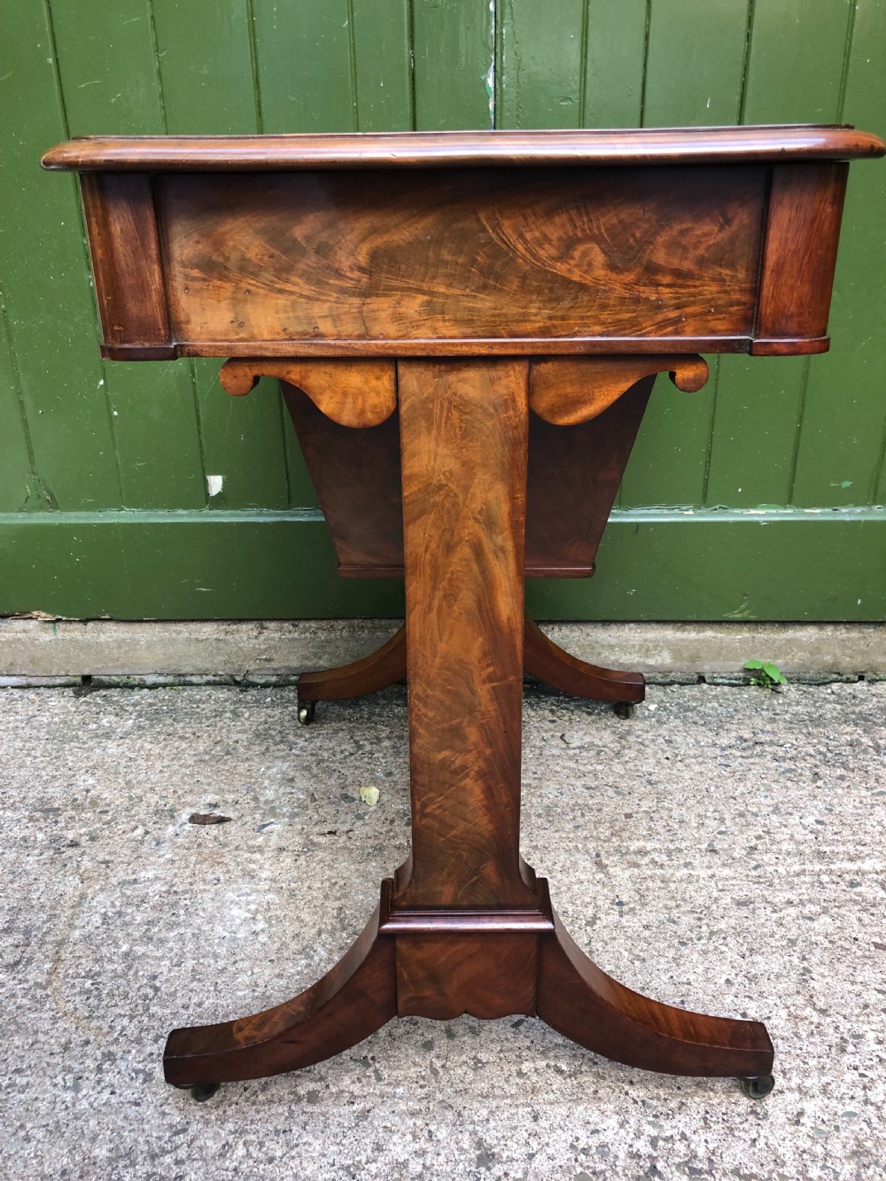 A George IV mahogany work table featuring a single drawer with turned knobs, a tapered lower well, carved trestle supports, and brass castors. View IX