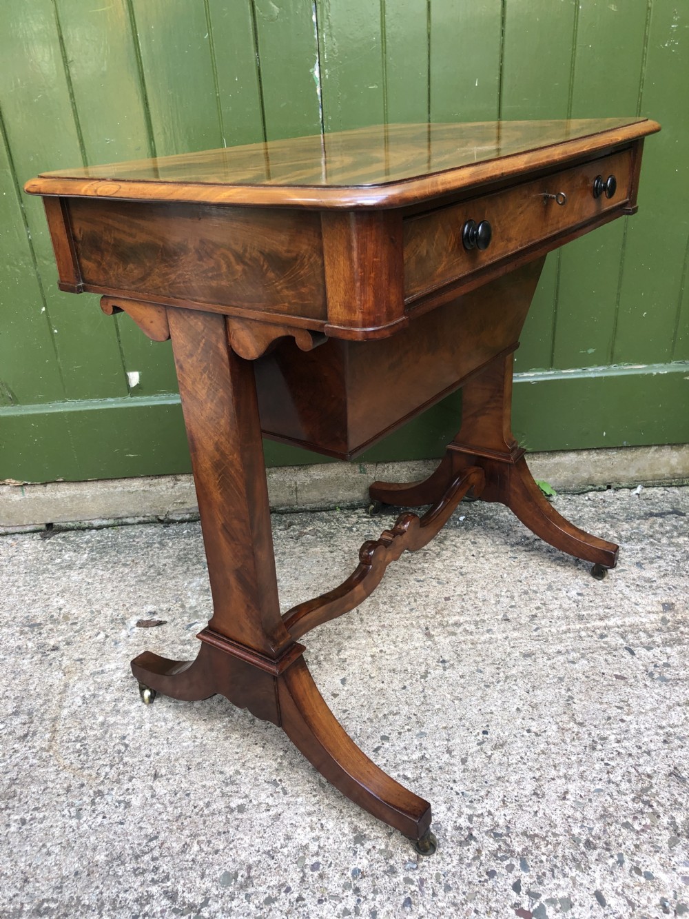 A George IV mahogany work table featuring a single drawer with turned knobs, a tapered lower well, carved trestle supports, and brass castors. View XIV