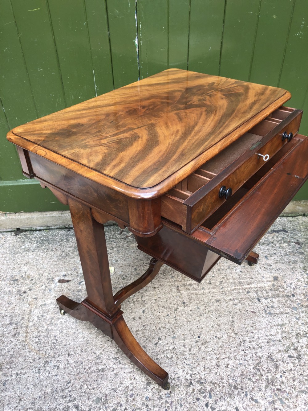 A George IV mahogany work table featuring a single drawer with turned knobs, a tapered lower well, carved trestle supports, and brass castors. View XVI