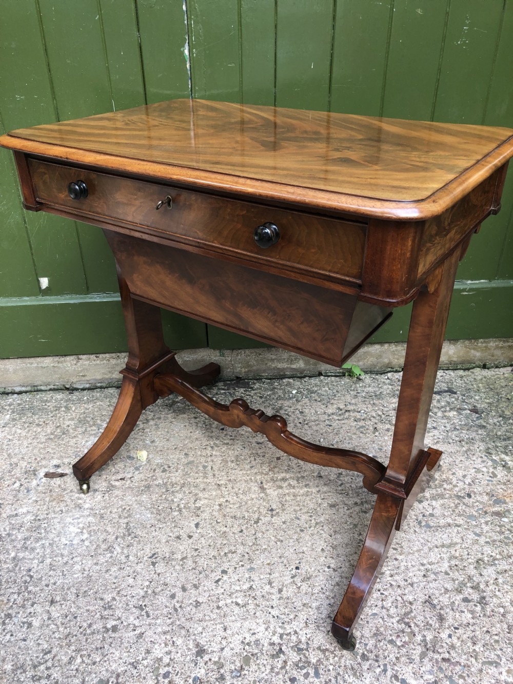 A George IV mahogany work table featuring a single drawer with turned knobs, a tapered lower well, carved trestle supports, and brass castors. View XVIII