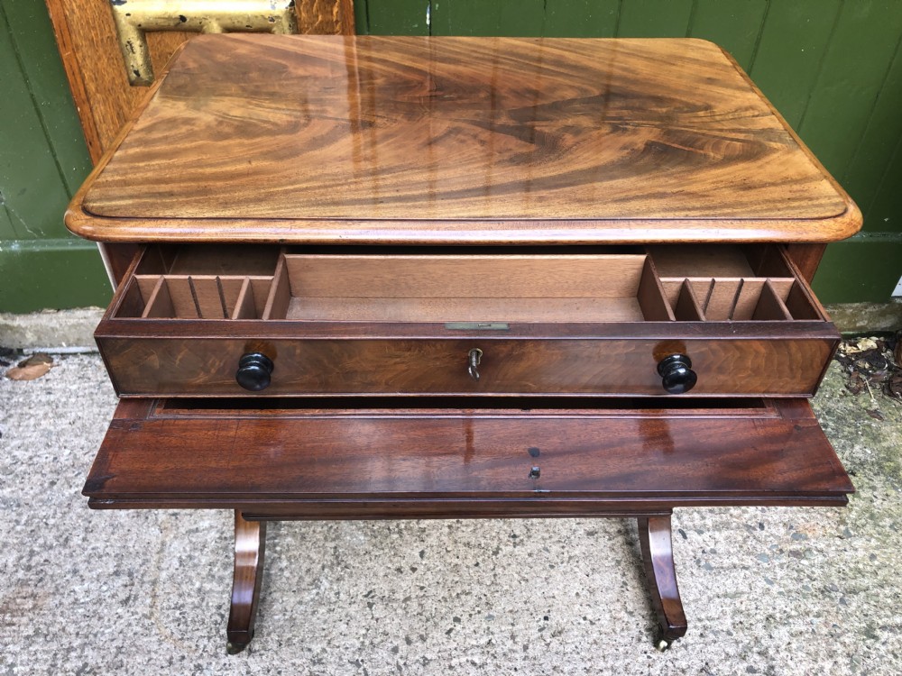 A George IV mahogany work table featuring a single drawer with turned knobs, a tapered lower well, carved trestle supports, and brass castors. View XXI