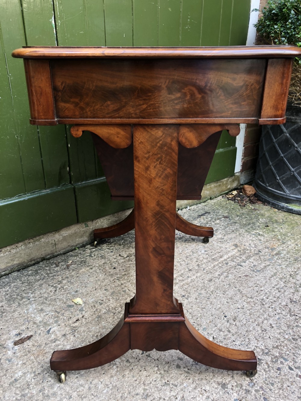 A George IV mahogany work table featuring a single drawer with turned knobs, a tapered lower well, carved trestle supports, and brass castors. View XXIV