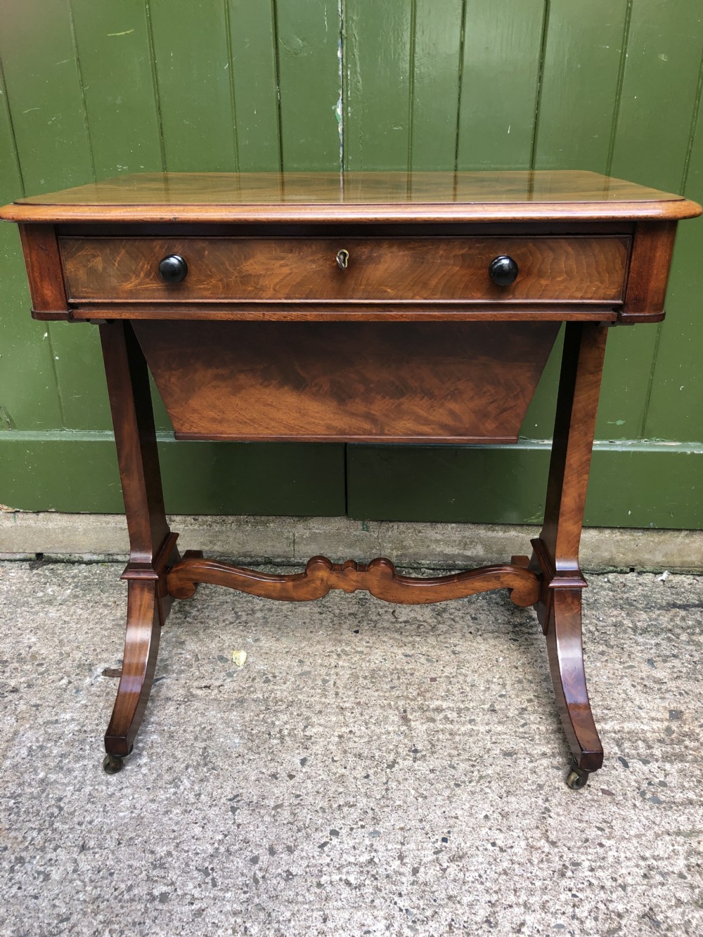 A George IV mahogany work table featuring a single drawer with turned knobs, a tapered lower well, carved trestle supports, and brass castors. View XXV