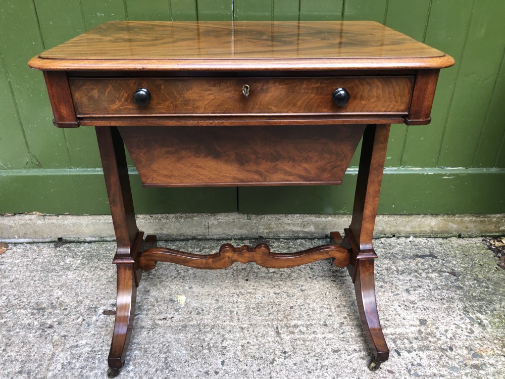 A George IV mahogany work table featuring a single drawer with turned knobs, a tapered lower well, carved trestle supports, and brass castors.