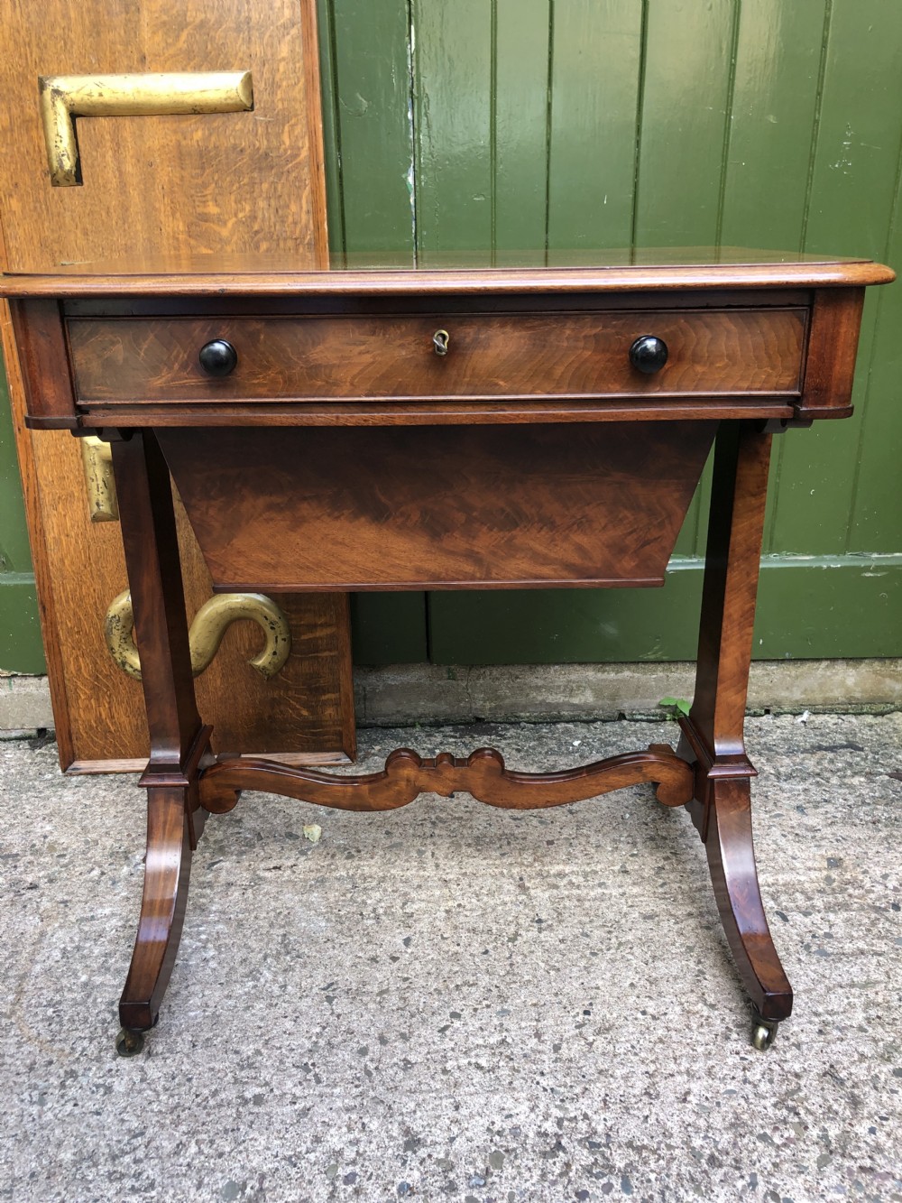 A George IV mahogany work table featuring a single drawer with turned knobs, a tapered lower well, carved trestle supports, and brass castors. View VI