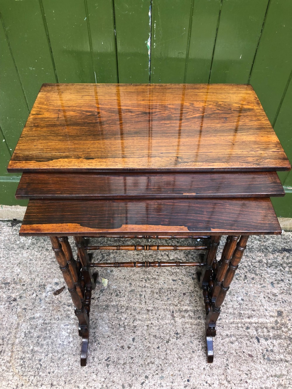 A set of three graduated Regency rosewood nesting tables featuring rectangular tops, slender turned spindle legs, and trestle bases. View X