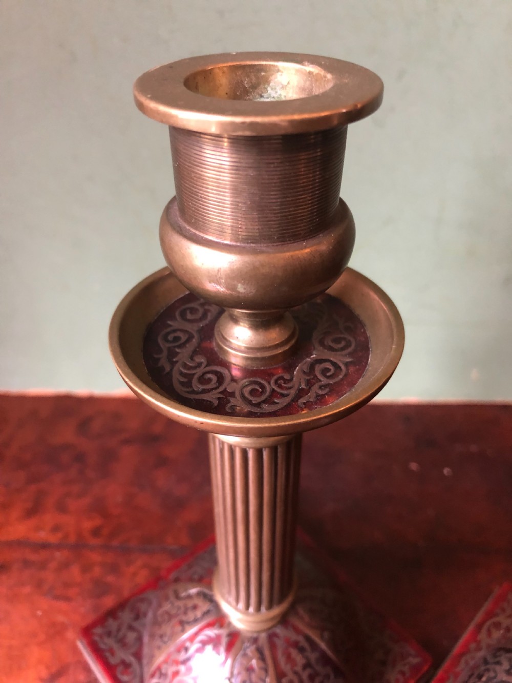 A pair of late 19th-century brass candlesticks featuring fluted columns supported by domed square bases inlaid with red tortoiseshell and engraved brass Boulle-work scroll motifs. View X