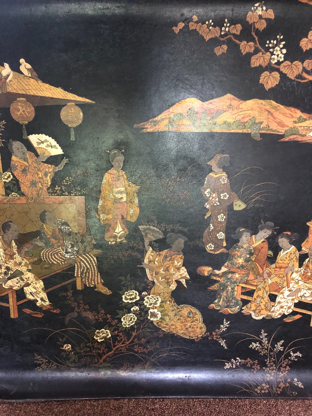 A mid-19th century rectangular black lacquer papier-mache tray decorated with hand-painted Japanese figures, traditional structures, and landscape scenery in gold and polychrome pigments. View V