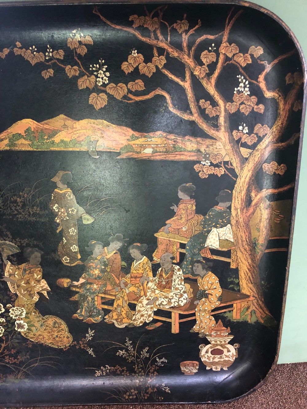A mid-19th century rectangular black lacquer papier-mache tray decorated with hand-painted Japanese figures, traditional structures, and landscape scenery in gold and polychrome pigments. View VI