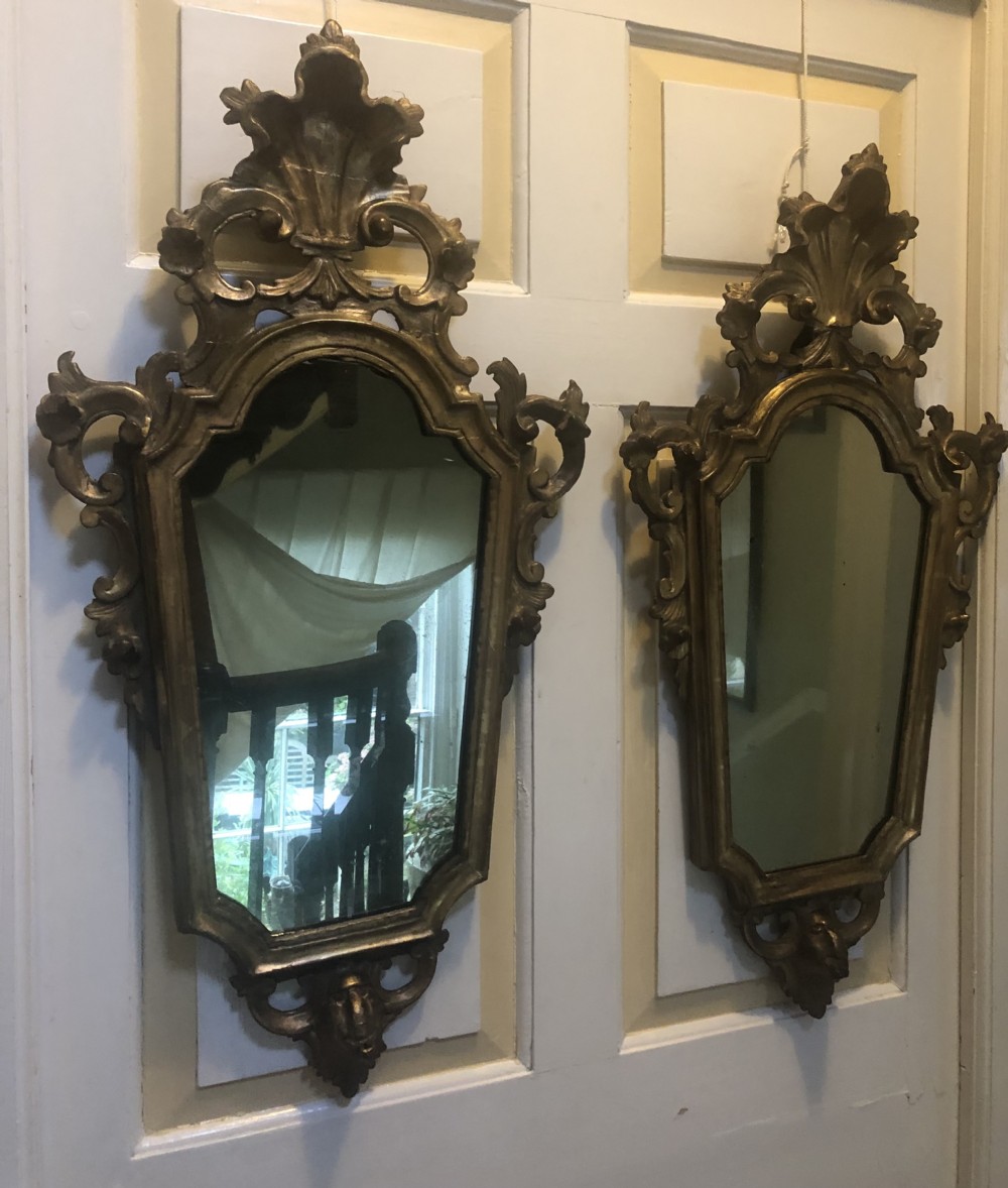 A pair of late eighteenth-century style carved giltwood pier mirrors featuring scrollwork cresting and shaped mirrored plates.