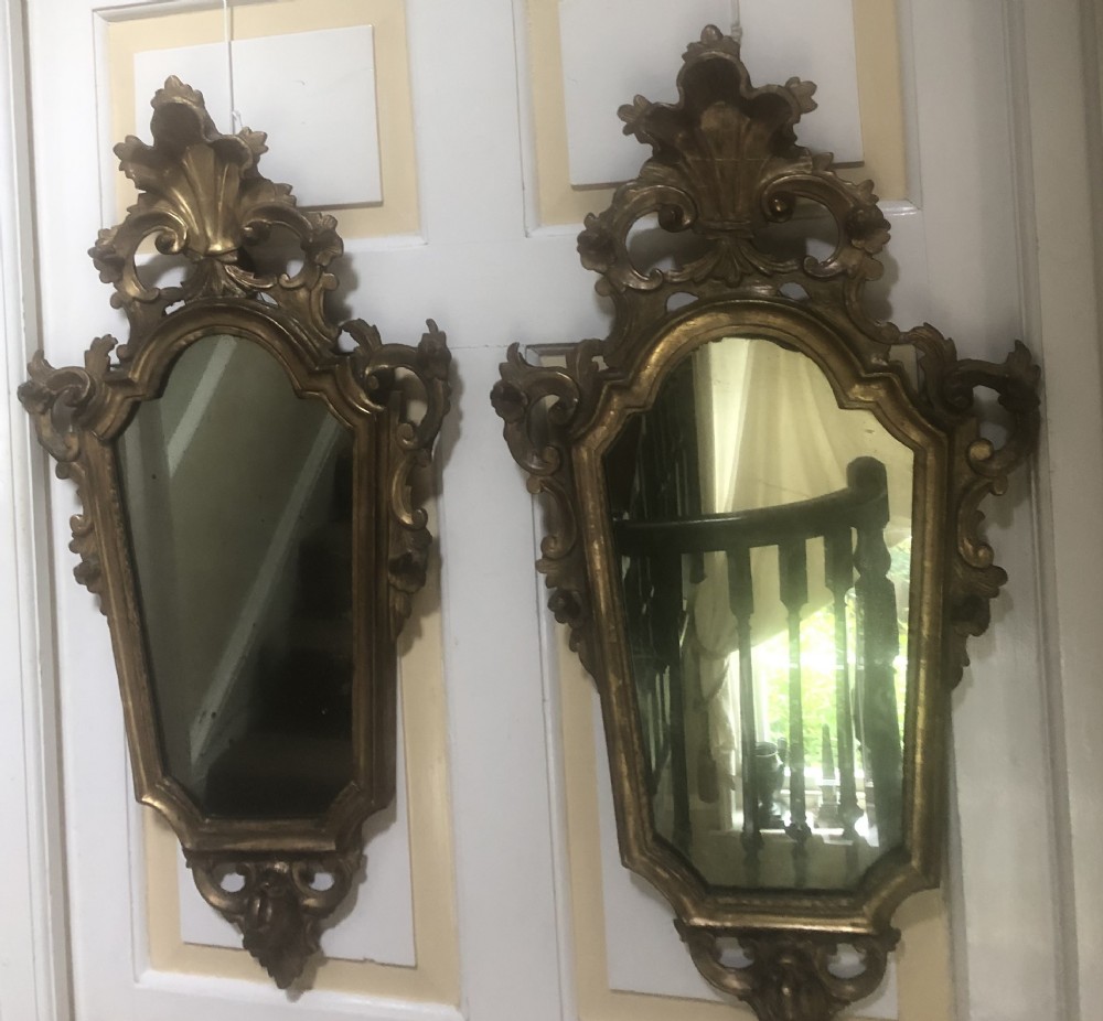A pair of late eighteenth-century style carved giltwood pier mirrors featuring scrollwork cresting and shaped mirrored plates. View II