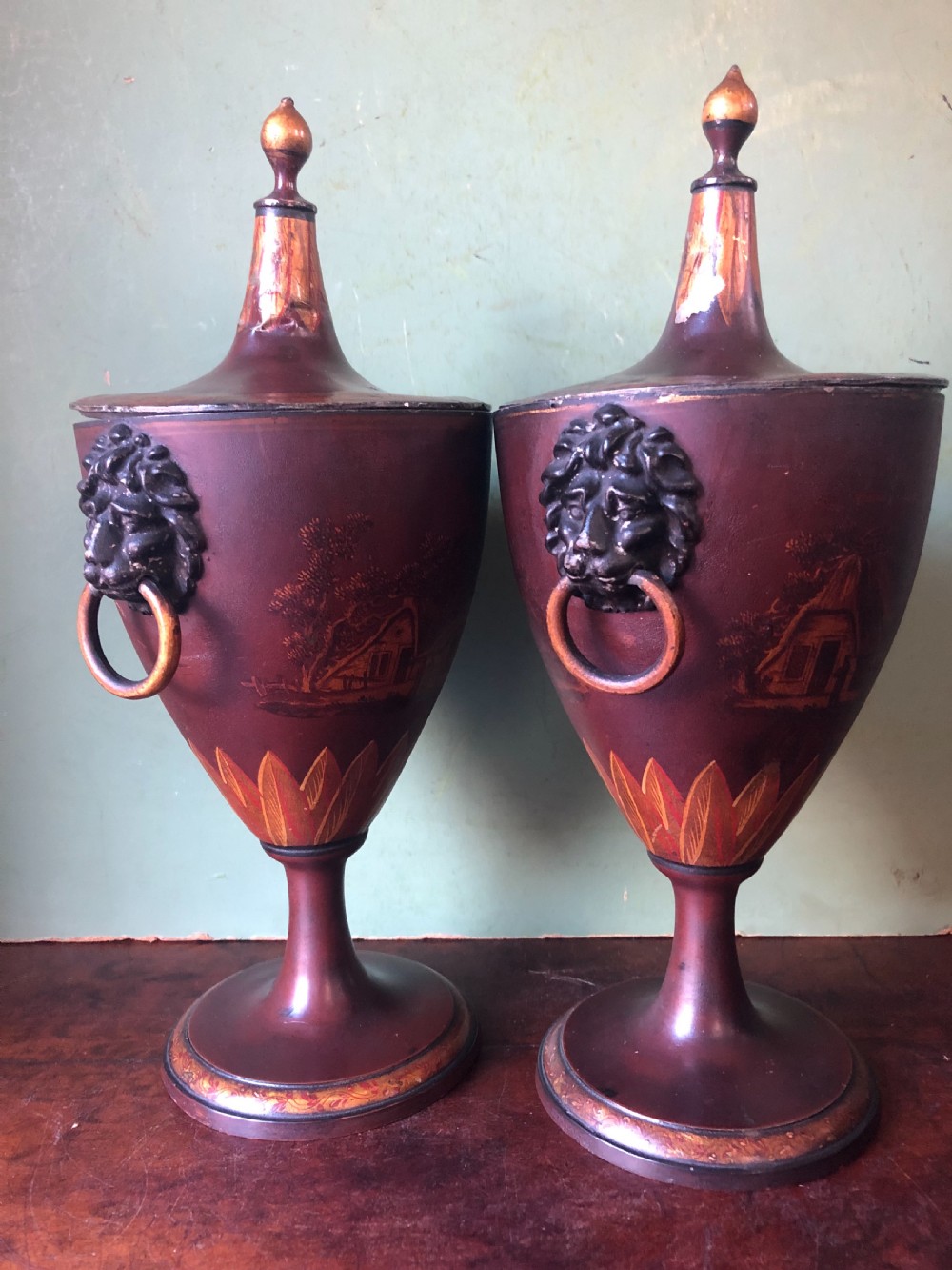 A pair of early 19th-century Dutch neoclassical chestnut urns in dark brown japanned pewter, painted with landscape scenes, leaf motifs, side ring handles, and tall finial lids. View II
